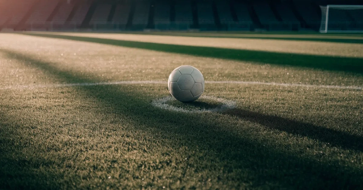 Un pallone da calcio sul dischetto del centrocampo di un prato, alla luce del mattino